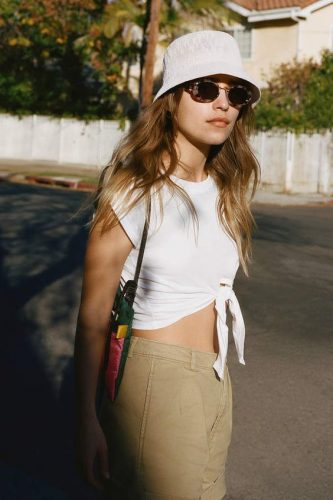 Mulher usa chapéu branco, óculos de sol, cropped branco e calça bege