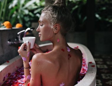 Sensual white woman with blonde hair drinking tea in bath. Amazing tanned lady doing spa with eyes closed and enjoying coffee.