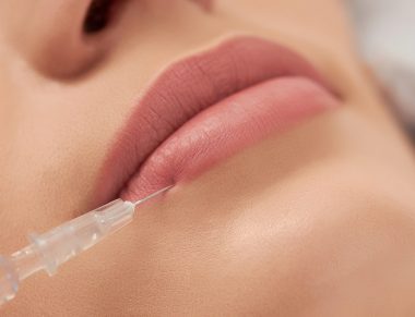 Close up of beautician in rubber gloves doing procedure lip augmentation for young beautiful woman in professional salon. Concept of beauty procedure with good mood.