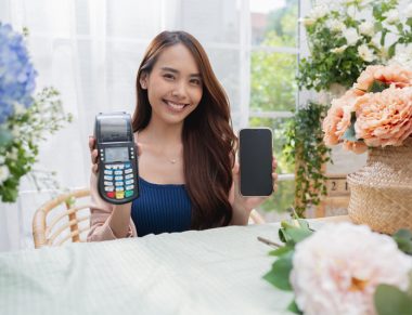 Portrait of a happy asian young adult florist floral shop with cheerful smiling hand show smartphone small business owner,Florist showing a smartphone while surrounded with flowers and plants