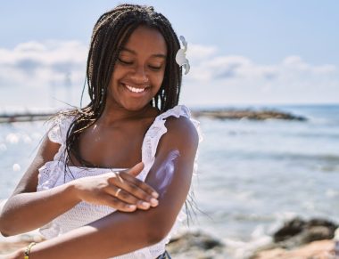 Young african american girl smiling happy using sunscreen lotion at the beach.